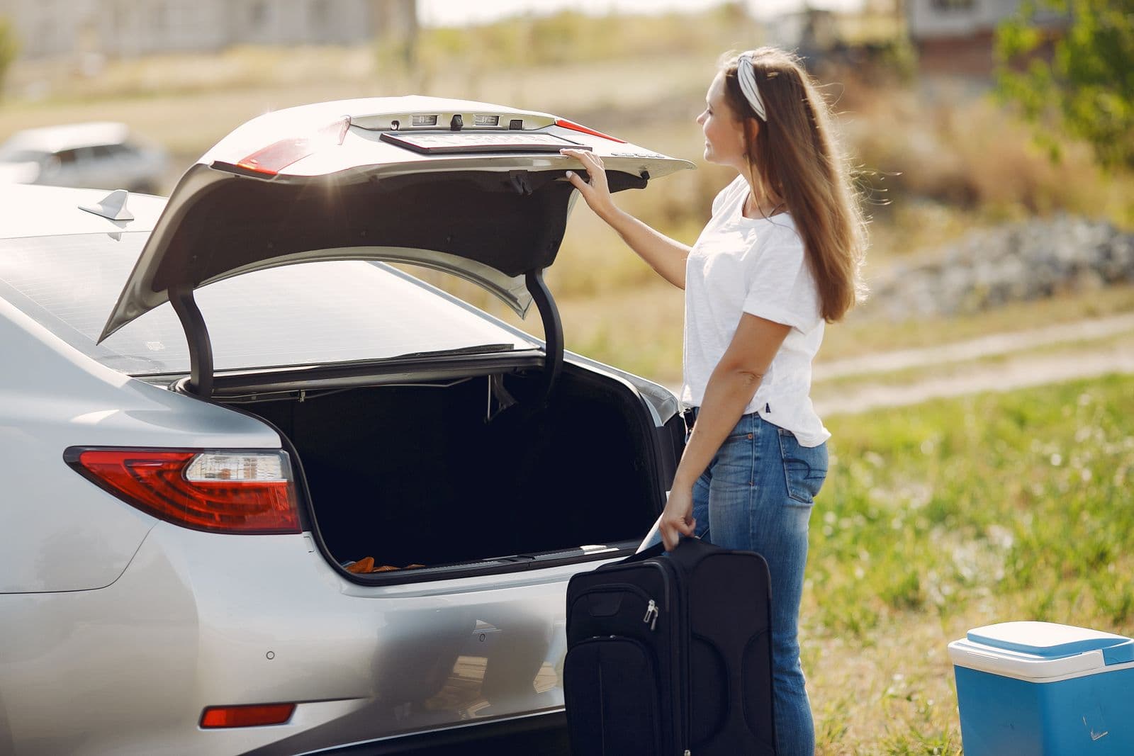 A traveller with her suitcase beside a car